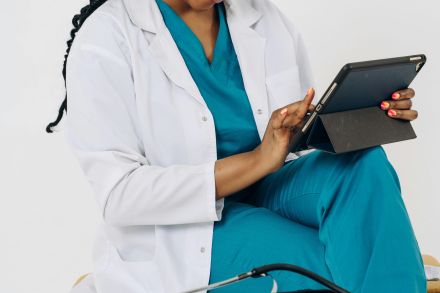 A woman in scrubs sitting on a stool with a tablet